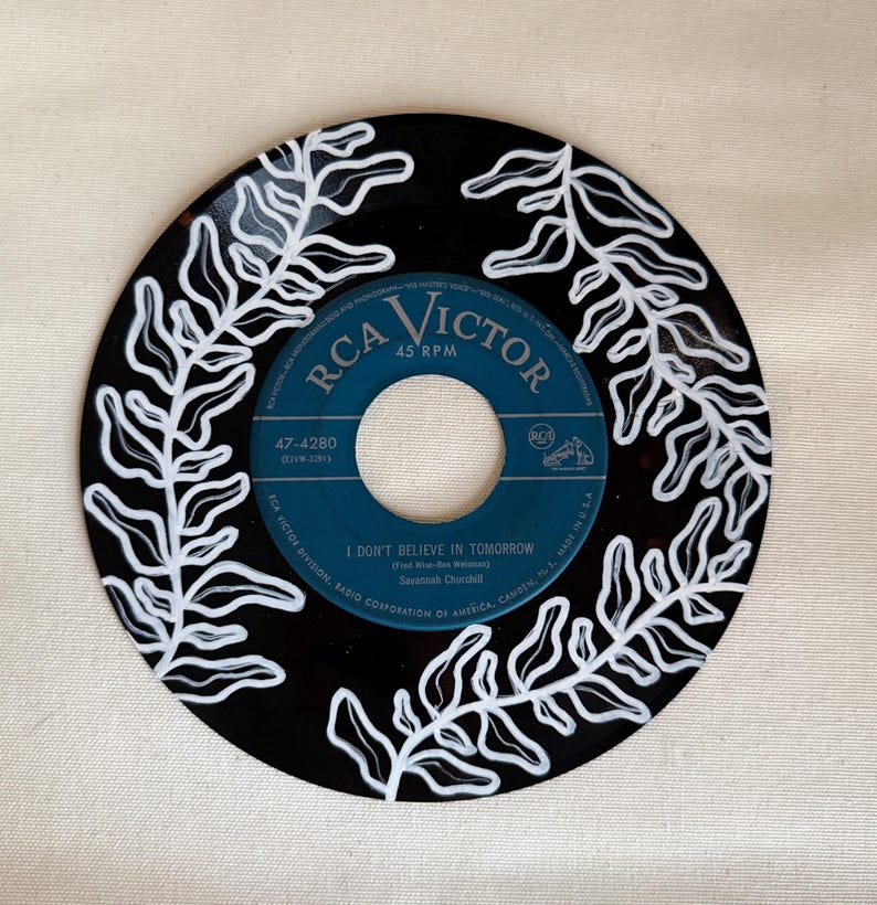 May include: A black vinyl record with white painted fern designs. The record label is blue and says "RCA Victor 45 RPM" and "47-4280". The song title is "I Don't Believe In Tomorrow" by Savannah Churchill.