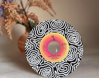 May include: A black and white vinyl record with a swirling pattern. The label is yellow, orange, and red with the text "BACKSIDE OF THIRTY" and "JOHN CONLEE".