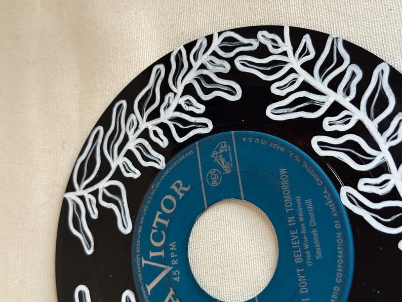 May include: A black vinyl record with a white fern design painted around the edge. The label is blue and says "Victor 45 RPM" and "I Don't Believe in Tomorrow" by Savannah Churchill.