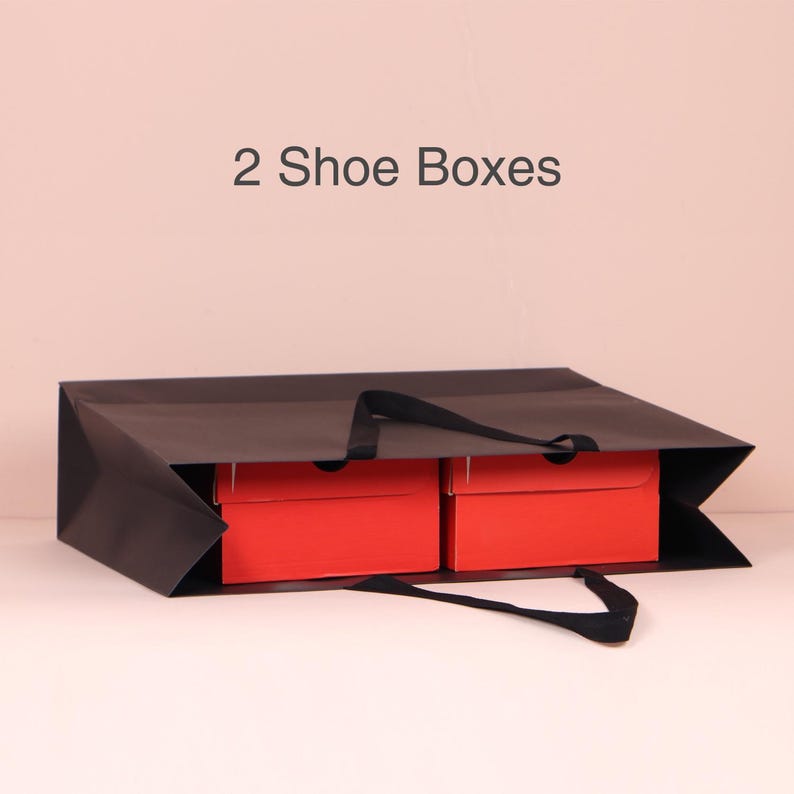 May include: A black paper shopping bag with two red shoe boxes inside. The bag has black handles and the text "2 Shoe Boxes" is above the bag.