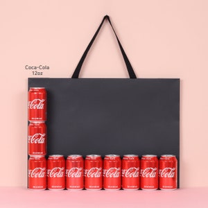May include: A display of Coca-Cola cans, each 12oz, arranged against a black background. The cans are red with white Coca-Cola branding. The arrangement includes a vertical stack of three cans and a horizontal row of seven cans.