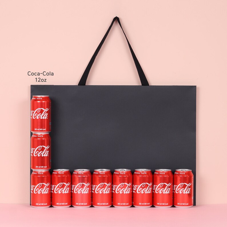 May include: A display of Coca-Cola cans, each 12oz, arranged against a black background. The cans are red with white Coca-Cola branding. The arrangement includes a vertical stack of three cans and a horizontal row of seven cans.