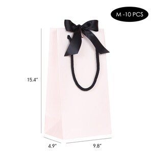 May include: A light pink gift bag with a black satin bow and black rope handles. The bag is 15.4 inches tall, 9.8 inches wide, and 4.9 inches deep. The text "M - 10 PCS" is in a black oval.