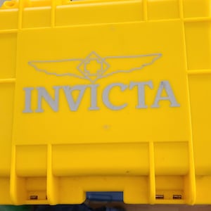 May include: Bright yellow rectangular case with the brand name "INVICTA" in gray lettering. The case has a hinged lid and a gray logo above the brand name. The case is made of a durable plastic material.