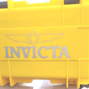 May include: A bright yellow hard case with a silver Invicta logo and a winged emblem. The case is made of durable plastic and has a secure latch.