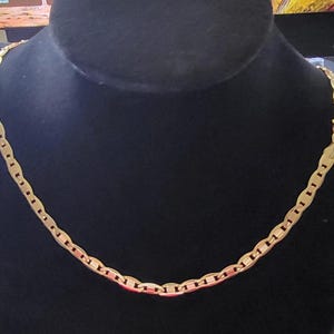 Op de afbeelding: Een gouden ketting met een plat, ovaalvormig schakellinkontwerp.
