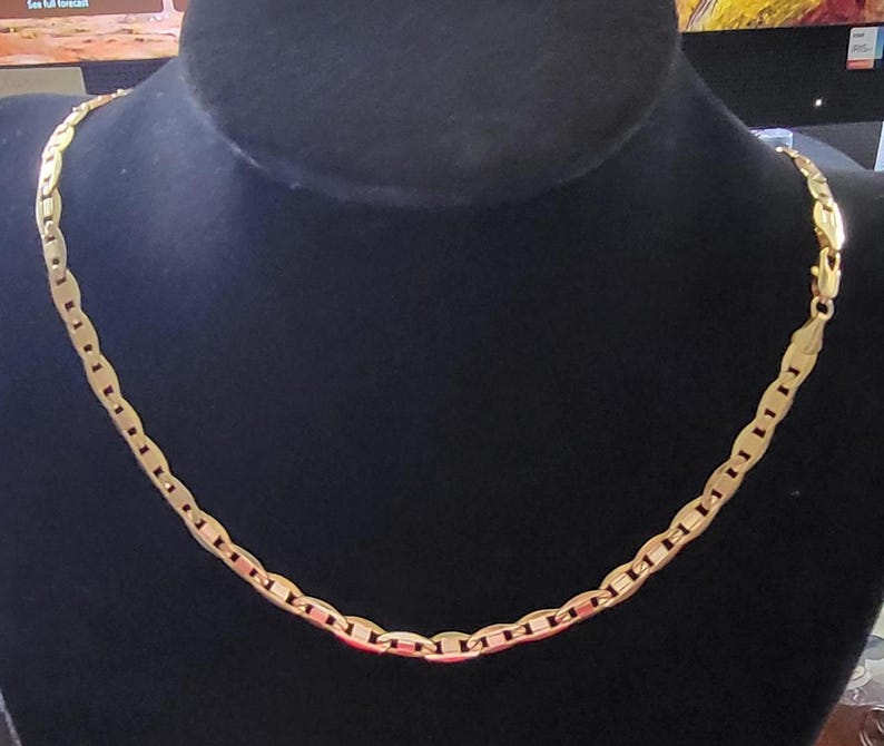 Op de afbeelding: Een gouden ketting met een plat, ovaalvormig schakellinkontwerp.