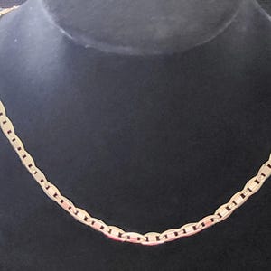 Op de afbeelding: Een gouden ketting met een ankerketting ontwerp. De ketting ligt op een zwarte displaystandaard.