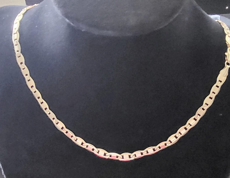 Op de afbeelding: Een gouden ketting met een ankerketting ontwerp. De ketting ligt op een zwarte displaystandaard.