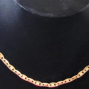 Op de afbeelding: Een gouden ketting met een ankerketting ontwerp. De ketting ligt op een zwarte achtergrond.