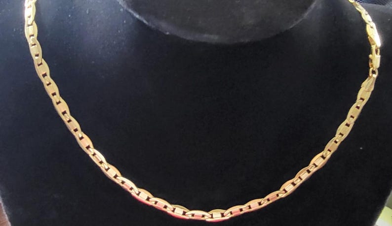 Op de afbeelding: Een gouden ketting met een ankerketting ontwerp. De ketting ligt op een zwarte achtergrond.