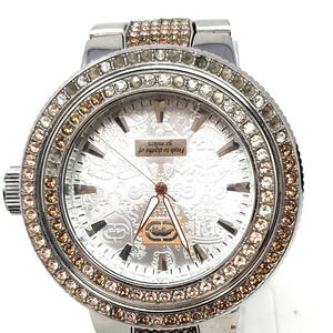 May include: A silver-toned wristwatch with a round face, adorned with clear and brown crystals around the bezel and on the band. The watch face has a patterned design and the text "Fresh to depths of 50 meters".