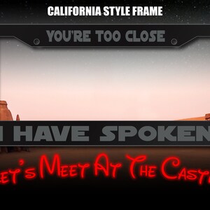 May include: A black metal license plate frame with the text "YOU'RE TOO CLOSE" and "I HAVE SPOKEN" in gray lettering. The text "LET'S MEET AT THE CASTLE" is in red lettering below the frame.