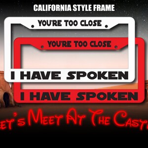 May include: Two red and white California license plate frames with the text "You're too close" and "I have spoken" in black. The frames are on a desert background with the text "Let's meet at the castle" in red.