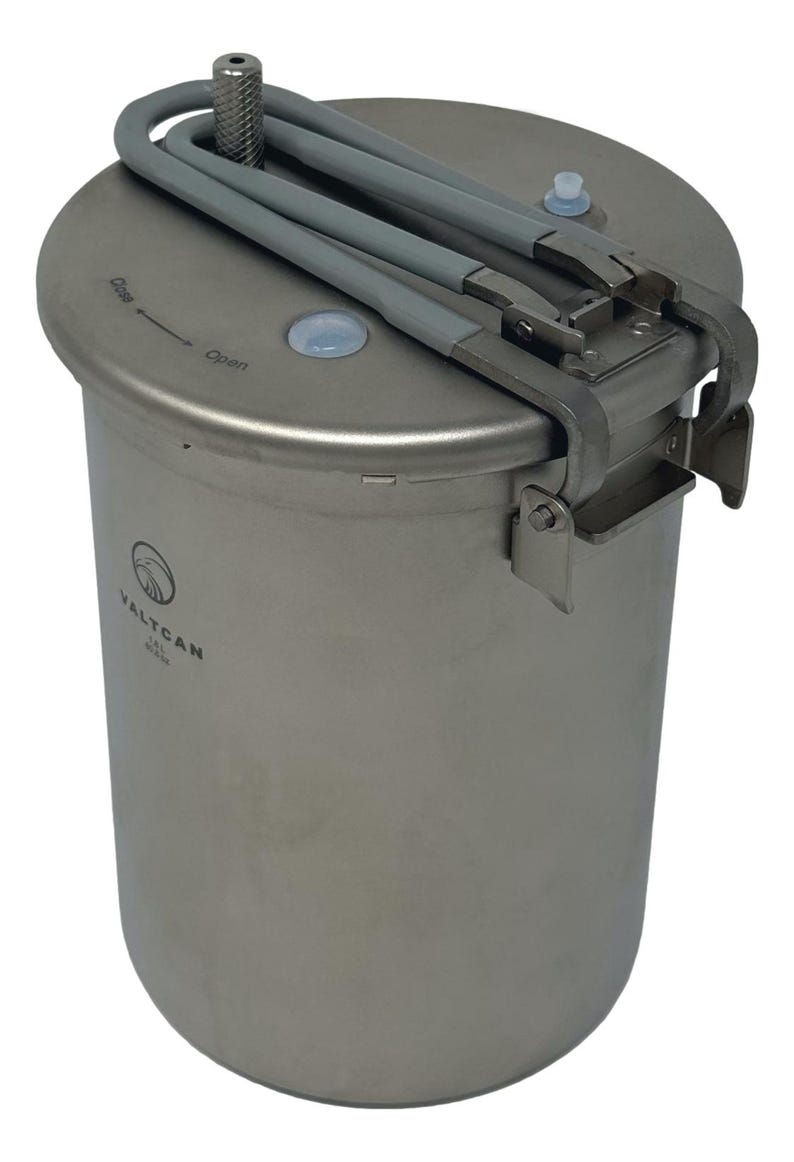 May include: A stainless steel VALTCAN container with a hinged lid and gray handles. The lid has a directional arrow indicating "Open" and "Close". The container has a cylindrical shape and a logo on the side.