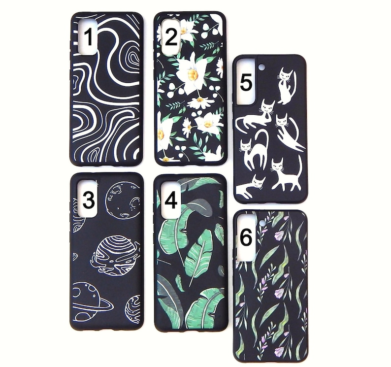 May include: A collection of six black phone cases with various designs. The designs include white swirls, white flowers, white cats, planets, green leaves, and purple and green foliage. The cases are rectangular with rounded corners.
