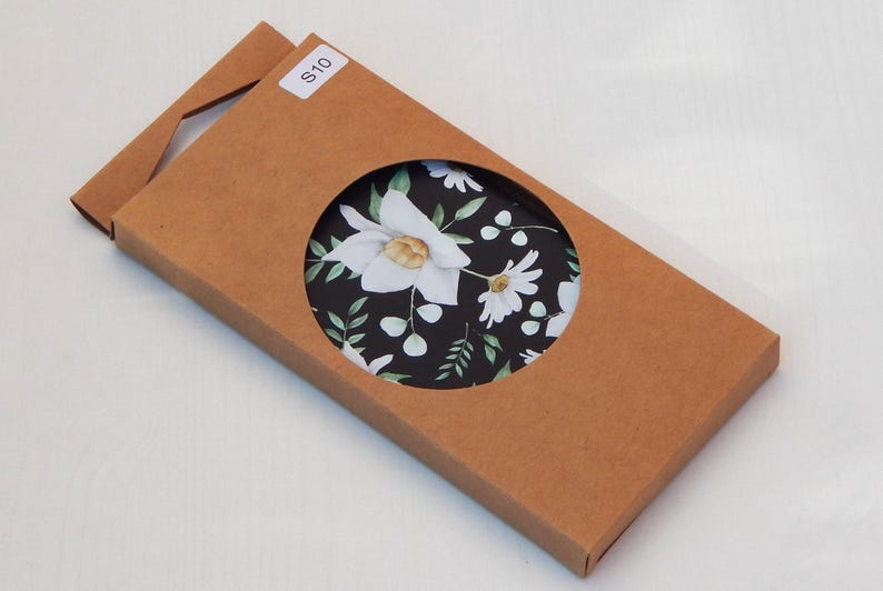 May include: A brown cardboard box with a circular cutout revealing a floral pattern. The pattern features white flowers and green leaves on a black background. A small white sticker with the text "S10" is on the box.