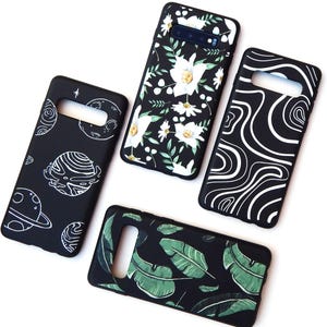 May include: Four black phone cases with unique designs. One case features white floral patterns, another has green leaves, a third displays white swirls, and the last showcases planets and stars in white. All cases have cutouts for the phone's camera and buttons.