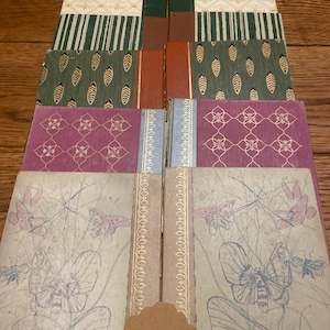 May include: A collection of ten hardcover books arranged in two columns. The covers feature diverse patterns including butterflies, geometric floral motifs, vertical stripes, and leaf designs in colors of cream, green, rust, purple, and light gray.
