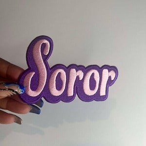 May include: Purple felt patch with the word "Soror" embroidered in pink.