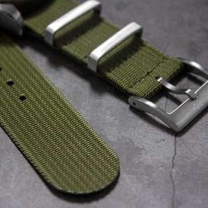 May include: A green nylon watch strap with a silver buckle. The strap has a textured surface and is designed for a watch with a 20mm lug width.