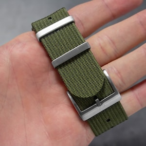 May include: A green nylon watch strap with silver hardware and the word "OSM" engraved on the buckle.
