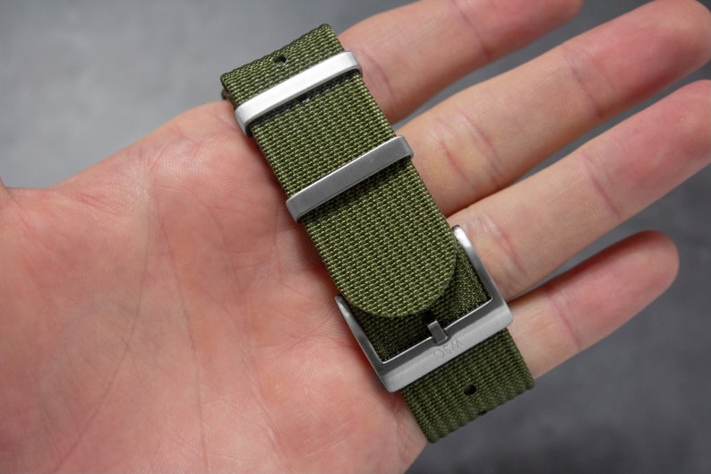 May include: A green nylon watch strap with silver hardware and the word "OSM" engraved on the buckle.