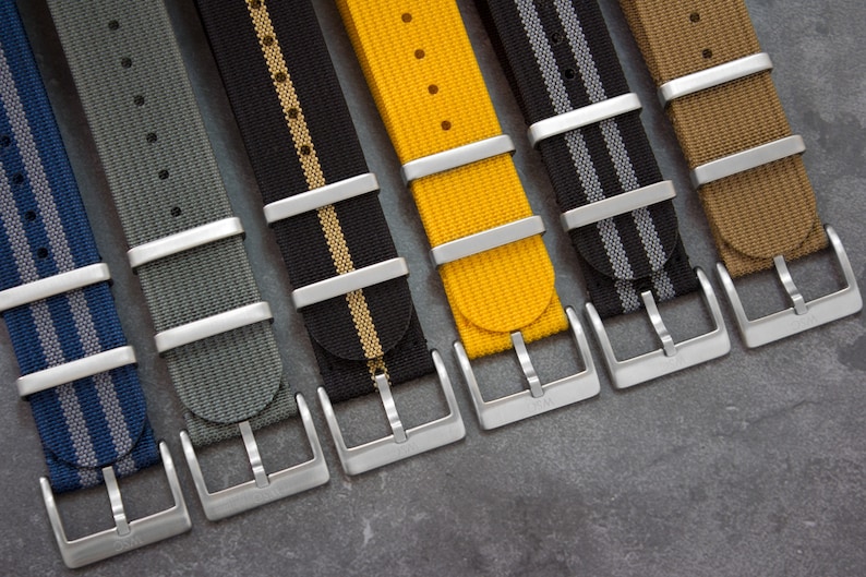 May include: Six different watch straps with silver buckles. The straps are made of nylon and have a striped pattern. The colors of the straps are blue, gray, black, yellow, brown, and tan.