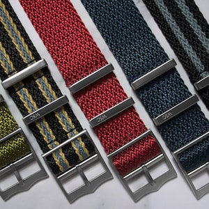 May include: Five different colored watch straps with silver buckles. The straps are made of woven nylon and have a striped pattern. The buckles are engraved with the letters "WSC".