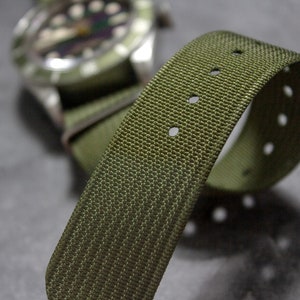 May include: A green nylon watch strap with multiple rows of stitching and holes for adjusting the size.