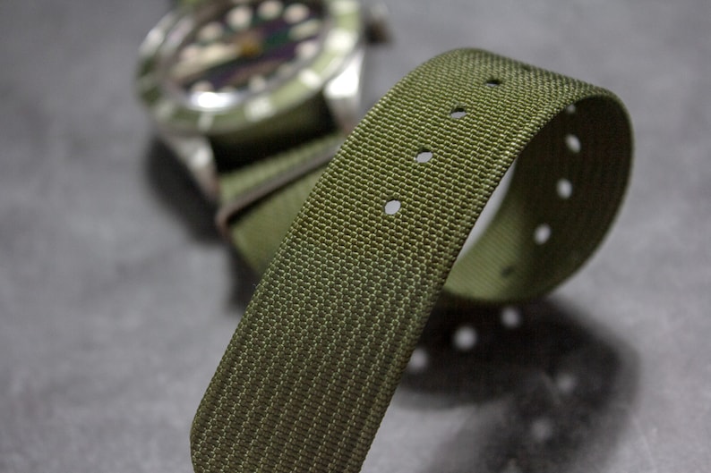 May include: A green nylon watch strap with multiple rows of stitching and holes for adjusting the size.