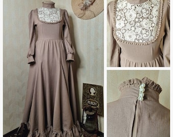 Puede incluir: Un vestido largo de color topo con mangas largas, cuello alto con borde de volantes, un peto de encaje floral blanco y dobladillo con volantes. La parte posterior del cuello se asegura con cuatro botones tipo perla sobre una abertura vertical.