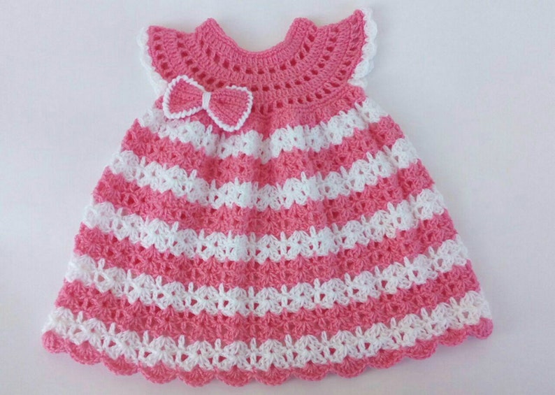 K&ouml;nnte beinhalten: Ein rosa-wei&szlig;es geh&auml;keltes Babykleid mit einer Schleife am Oberteil.