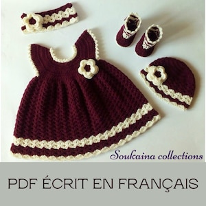 May include: A crocheted baby outfit set in burgundy and cream. The set includes a dress, hat, booties, and headband. The dress has a scalloped trim and a flower embellishment. The hat and booties also have scalloped trim and flower embellishments. The headband has a flower embellishment. The text "PDF ÉCRIT EN FRANÇAIS" is at the bottom of the image.