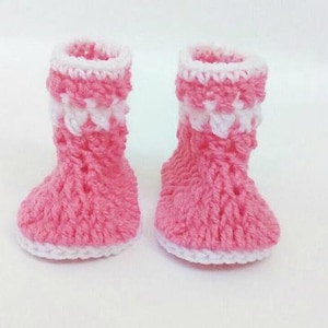 K&ouml;nnte beinhalten: Ein Paar rosa und wei&szlig;e geh&auml;kelte Babyschuhe. Die Schuhe haben einen wei&szlig;en Rand und ein rosa-wei&szlig;es Streifenmuster.