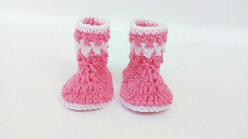 K&ouml;nnte beinhalten: Ein Paar rosa und wei&szlig;e geh&auml;kelte Babyschuhe. Die Schuhe haben einen wei&szlig;en Rand und ein rosa-wei&szlig;es Streifenmuster.