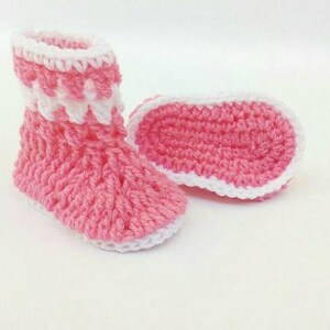 K&ouml;nnte beinhalten: Ein Paar rosa geh&auml;kelte Babyschuhe mit wei&szlig;em Besatz. Die Schuhe haben ein weiches, strukturiertes Gestrick und sind perfekt, um kleine F&uuml;&szlig;e warm zu halten.