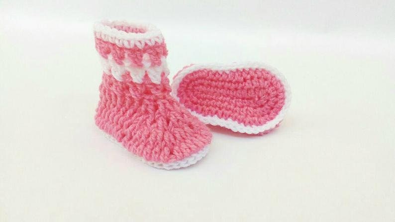 K&ouml;nnte beinhalten: Ein Paar rosa geh&auml;kelte Babyschuhe mit wei&szlig;em Besatz. Die Schuhe haben ein weiches, strukturiertes Gestrick und sind perfekt, um kleine F&uuml;&szlig;e warm zu halten.