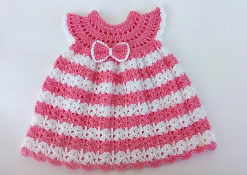 K&ouml;nnte beinhalten: Ein rosa-wei&szlig;es geh&auml;keltes Babykleid mit einer Schleife am Ausschnitt.