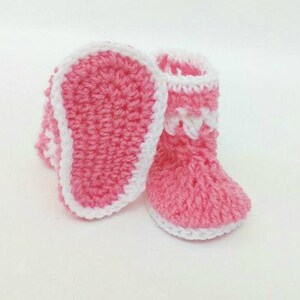 K&ouml;nnte beinhalten: Ein Paar rosa geh&auml;kelte Babyschuhe mit wei&szlig;em Besatz. Die Schuhe haben ein schlichtes Design und sind perfekt f&uuml;r ein Neugeborenes.