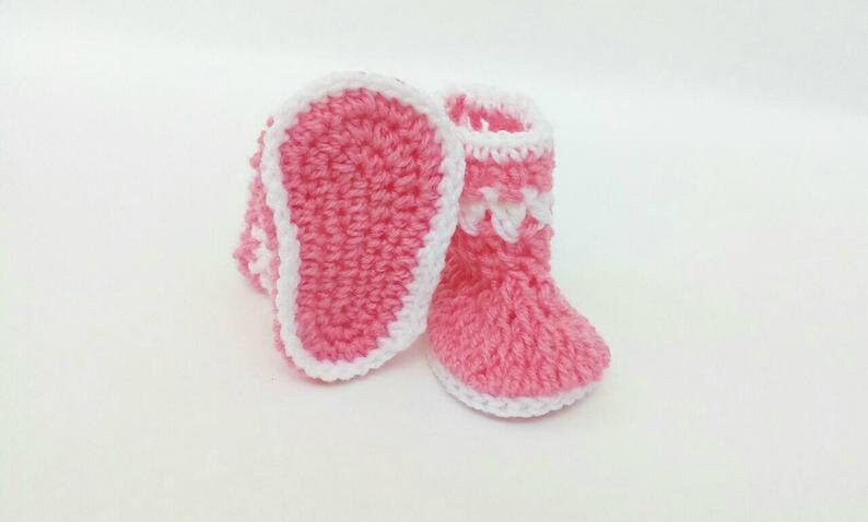 K&ouml;nnte beinhalten: Ein Paar rosa geh&auml;kelte Babyschuhe mit wei&szlig;em Besatz. Die Schuhe haben ein schlichtes Design und sind perfekt f&uuml;r ein Neugeborenes.