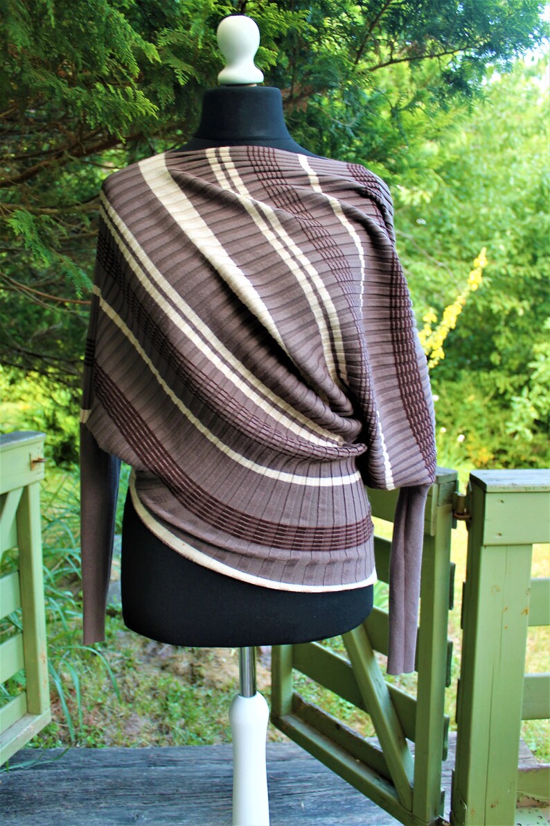 May include: A brown and white striped sweater with a draped design. The sweater is on a white mannequin and has long sleeves.