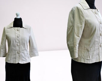 May include: A cream-colored blazer with a button-up front and two pockets. The blazer has a collar and three-quarter sleeves.