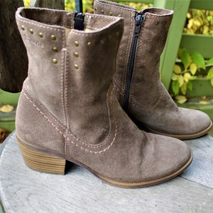 May include: A pair of brown suede ankle boots with a zipper on the side and a decorative row of studs on the back. The boots have a low block heel.