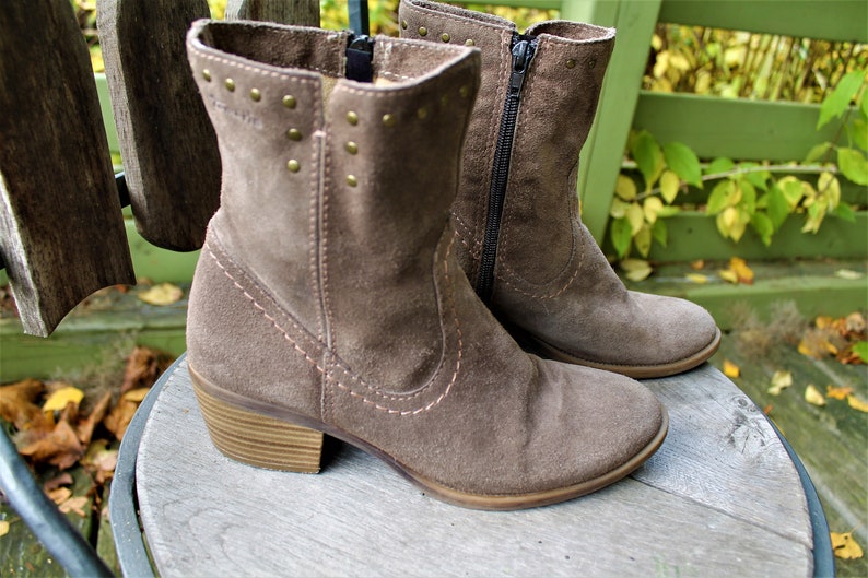 May include: A pair of brown suede ankle boots with a zipper on the side and a decorative row of studs on the back. The boots have a low block heel.
