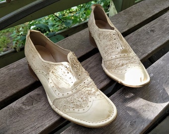 May include: Two pairs of off-white leather shoes with a brogue design. The shoes have a textured surface and a lace-up closure.