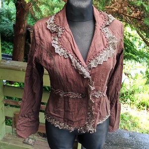 May include: A brown jacket with a lace trim and beaded accents. The jacket has a button closure and long sleeves.