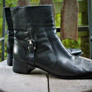 May include: A pair of black leather ankle boots with a buckle detail on the side. The boots have a low block heel and a square toe.
