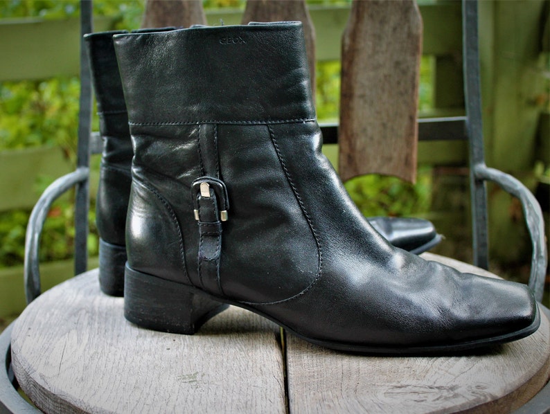 May include: A pair of black leather ankle boots with a buckle detail on the side. The boots have a low block heel and a square toe.