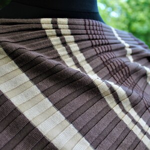 May include: Brown and white striped fabric with a ribbed texture. The fabric is folded and draped over a form.